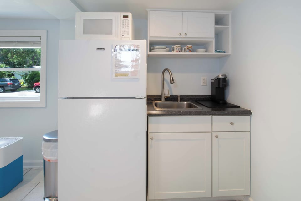 Your compact kitchenette has everything you need: a full fridge, microwave, sink, and coffee maker, all in crisp white and light blue. Simple, clean, and ready for your morning coffee or quick snack.