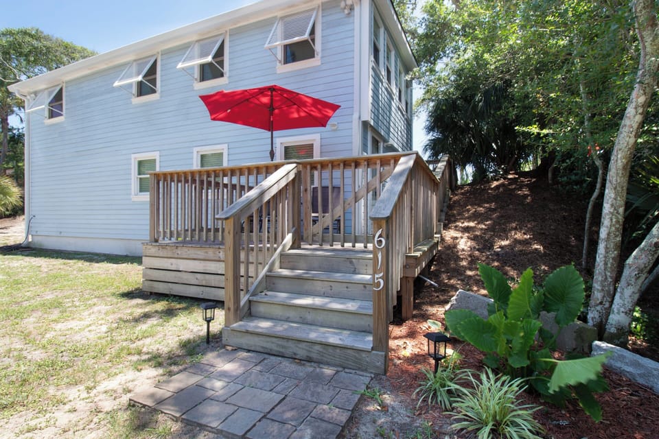 A welcoming wooden stairway leads to your elevated deck with bright red umbrella, perfect for morning coffee surrounded by tropical greenery and sunshine.