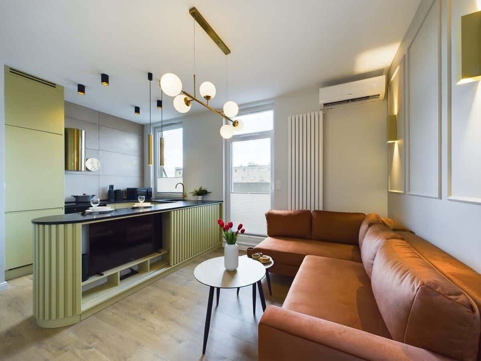 Bright kitchen and lounge space with soft colors, wooden floor, and round lighting fixtures.