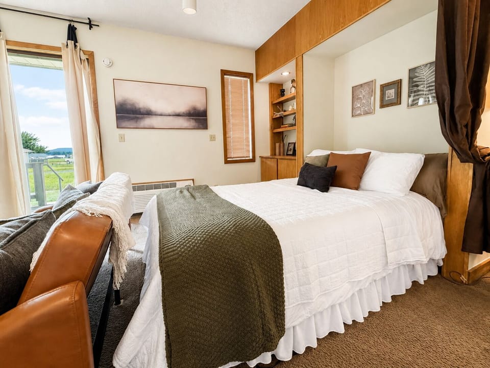 Sink into crisp linens and cozy textures in your sunlit bedroom, where natural wood tones create a warm retreat. Wake to peaceful rural views through your window and enjoy thoughtful touches like custom shelving for your belongings.