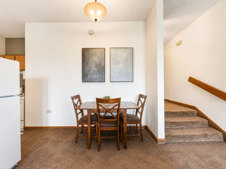 Your cozy dining area awaits with warm wood tones and inviting seating, perfect for sharing meals together. The open layout connects kitchen and stairway, creating a welcoming flow through your home.