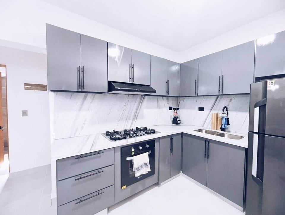 This modern kitchen and living room area seamlessly combines functionality and style, creating an inviting space for both cooking and relaxation. The sleek design features contemporary cabinetry and high-end appliances.