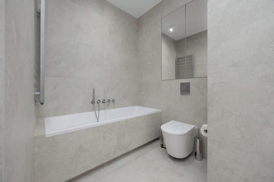 Elegant bathroom with bathtub, wall-mounted toilet, and clean grey tiles.