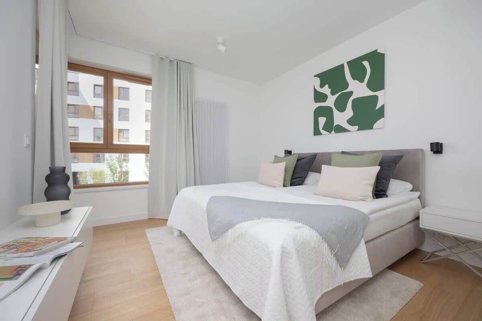 Bright bedroom with double bed, neutral tones, wall art, and natural light from large window.
