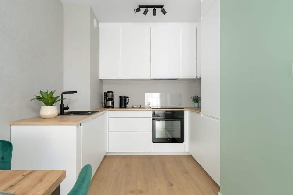 A functional, modern kitchen in pure white tones, equipped with integrated appliances and a clean, uncluttered worktop, emphasizing simplicity and efficiency.