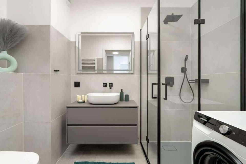 A sleek gray-tiled bathroom with a walk-in shower and washing machine.