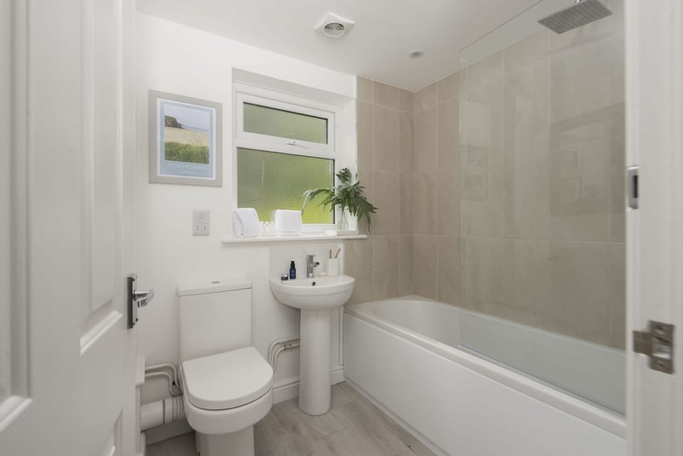 Castaways, Porthtowan. First Floor: The family bathroom offers a bath and overhead shower, wash basin, heated towel rail and WC