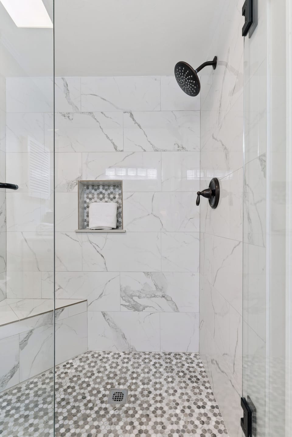 Luxurious marble-look tiles and mosaic details create a spa-like ambiance where you can unwind under the rain-style showerhead in this elegantly designed walk-in shower.