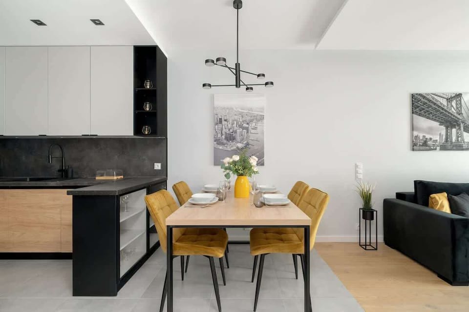 A bright kitchen and dining area with wooden accents and a modern light fixture above the table. The style is clean and Scandinavian-inspired.