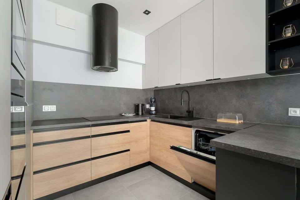 A modern kitchen with wooden cabinets, black countertops, and sleek appliances. The space is well-lit and efficiently designed.
