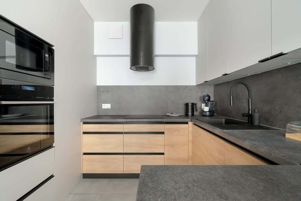 A sleek kitchen with light wooden cabinetry, a black countertop, and white walls. The design is simple, modern, and efficient.