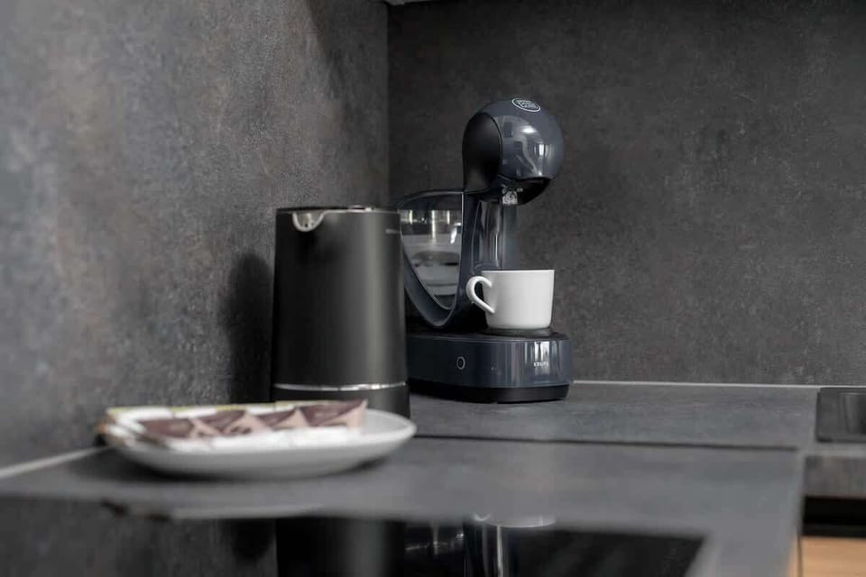 A small coffee corner with a black coffee machine and cups. The dark aesthetic gives it a trendy, barista-style feel.