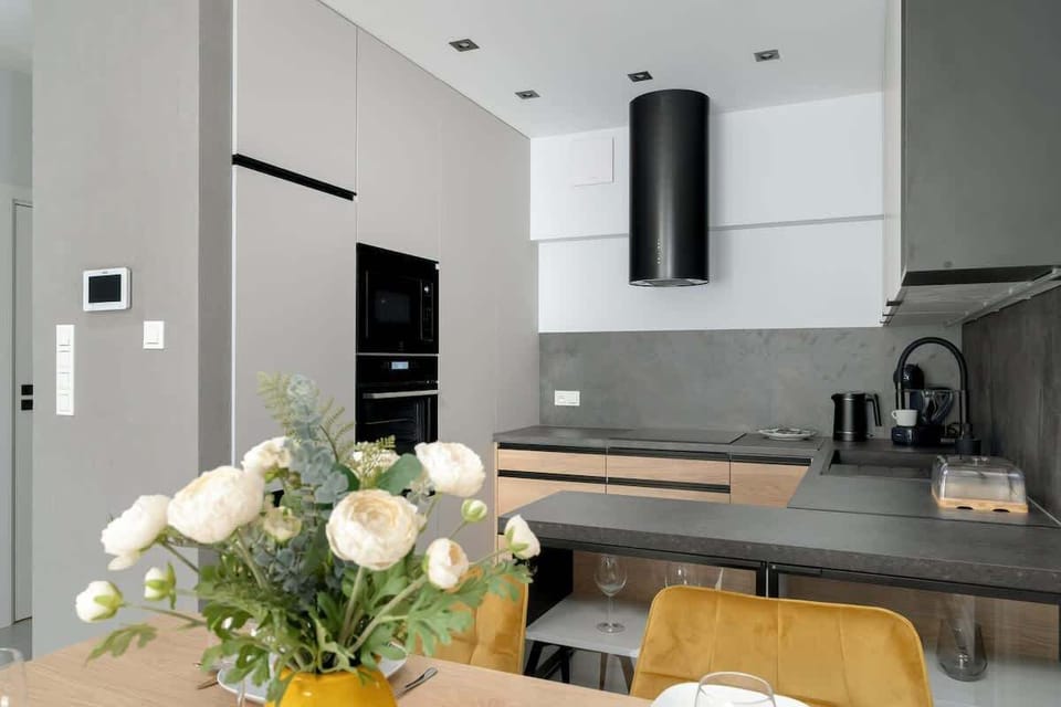 A dining area with modern tableware and white flowers on the table. The kitchen background features sleek finishes and clean design.