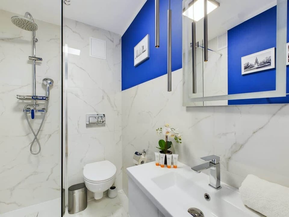 Another modern bathroom featuring a glass shower, sleek sink, and bright lighting. Blue accents stand out against the white tilework.