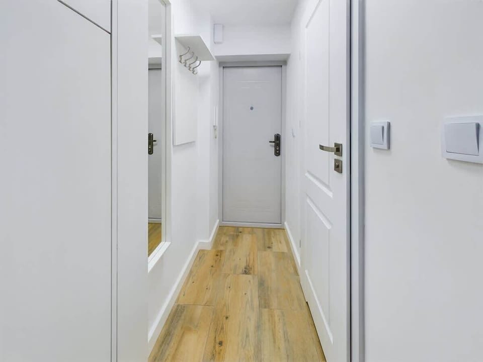 A narrow hallway with white storage cabinets and light wooden floors. It leads into other bright, modern spaces.