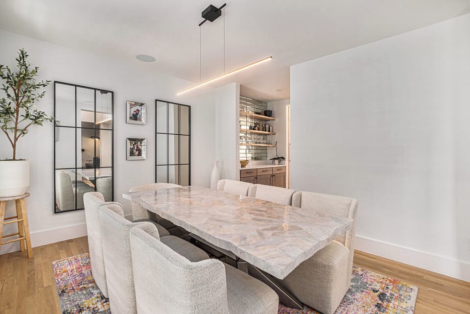 - Dine in elegance at this stunning stone table with eight cozy upholstered chairs
- Sleek lighting and a mirrored accent wall create a sophisticated ambiance
- Just steps away, the wet bar promises effortless entertaining