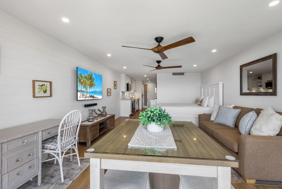 Picture yourself unwinding in this bright, coastal-inspired studio where cozy seating, a plush bed, and breezy ceiling fans create your perfect beach getaway retreat.