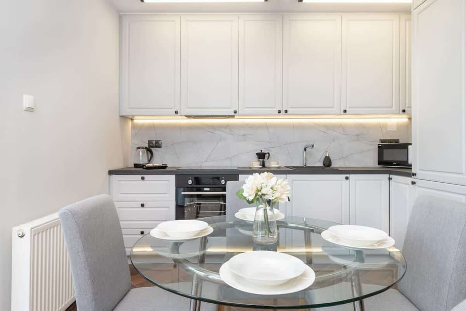 Dining Table – Round white table set with plates and glassware, next to kitchen cabinetry.

