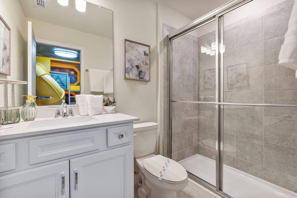 This bright bathroom boasts a sleek glass shower and a stylish white vanity with modern fixtures. Enjoy the inviting decor and subtle touches of color in the adjoining space for a refreshing atmosphere.
