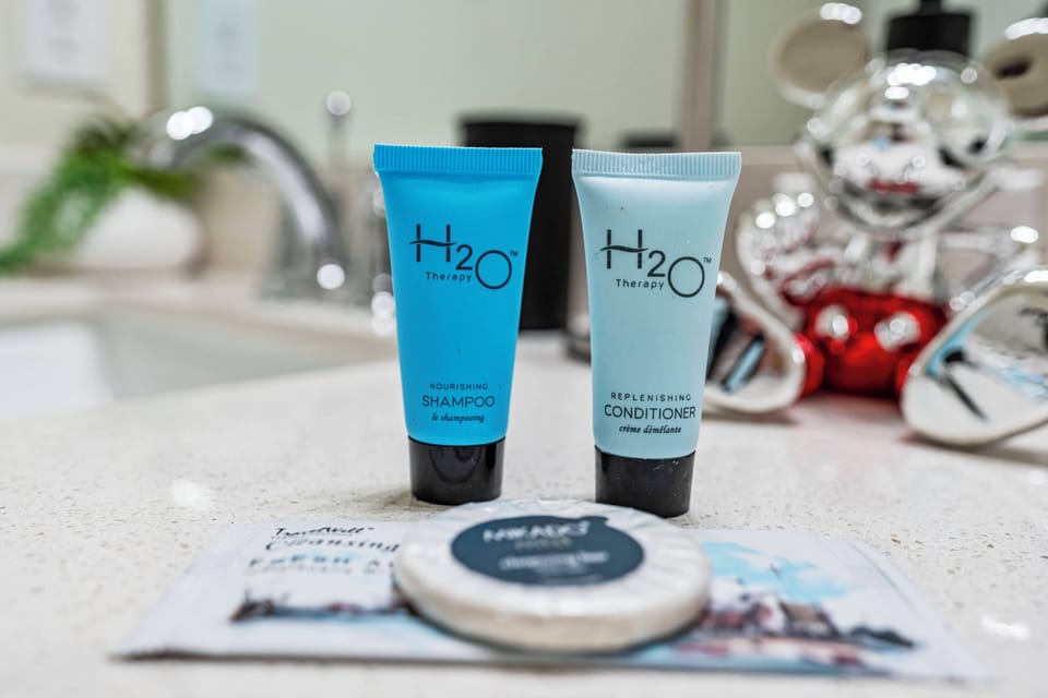 Experience a touch of luxury with premium H2O toiletries elegantly displayed on a sleek countertop, complemented by the soft glimmer of modern fixtures. Indulge in self-care while enjoying the tranquil ambiance of your escape.