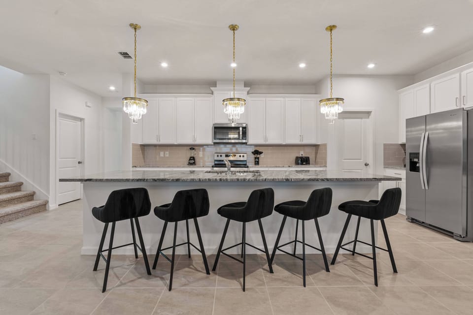 Welcome to a bright kitchen featuring sleek white cabinetry and a spacious granite island, ideal for gathering. The stylish black bar stools and elegant pendant lighting create an inviting space for meal prep and conversation.