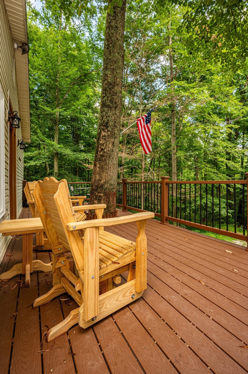 Wooden rocking chairs line the brown composite deck, wrapped around a mature tree beside black metal railings.