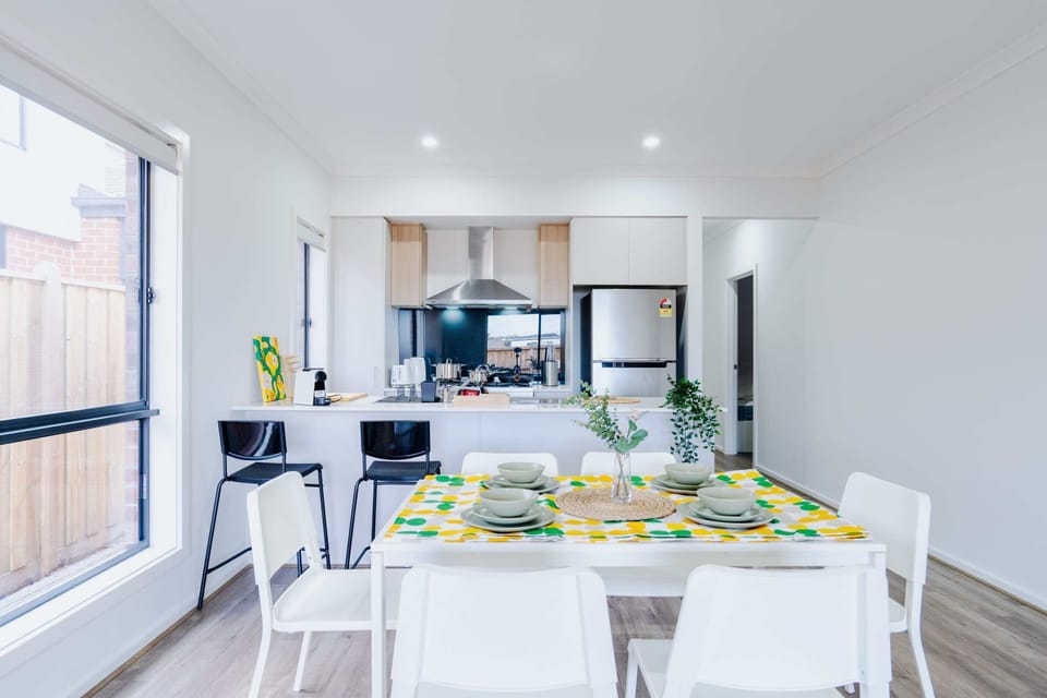 Modern open-plan kitchen and dining area with a table set for 6 and sleek kitchen appliances.