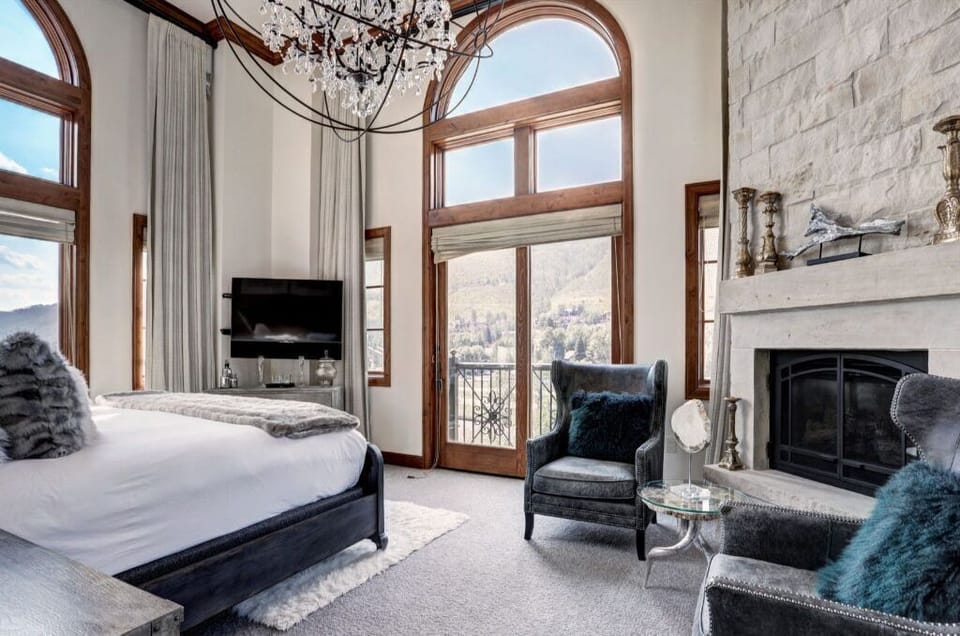Luxurious bedroom with a fireplace, chandelier, and large windows.