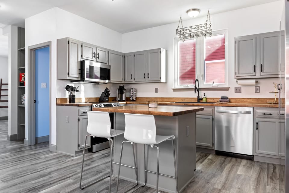A complete kitchen view highlights the breakfast island, range, microwave, dishwasher, sink, and countertop workspace.