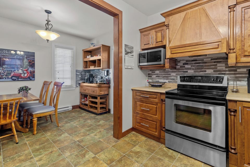 The dining area, adjacent to the kitchen, features a stylish table and chairs, perfect for family meals. The kitchen itself is equipped with modern appliances, beautiful wooden cabinetry, and a chic tile backsplash.