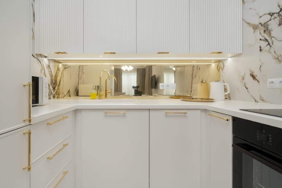 Modern kitchenette with light-colored cabinets, elegant lighting, and gold accents.