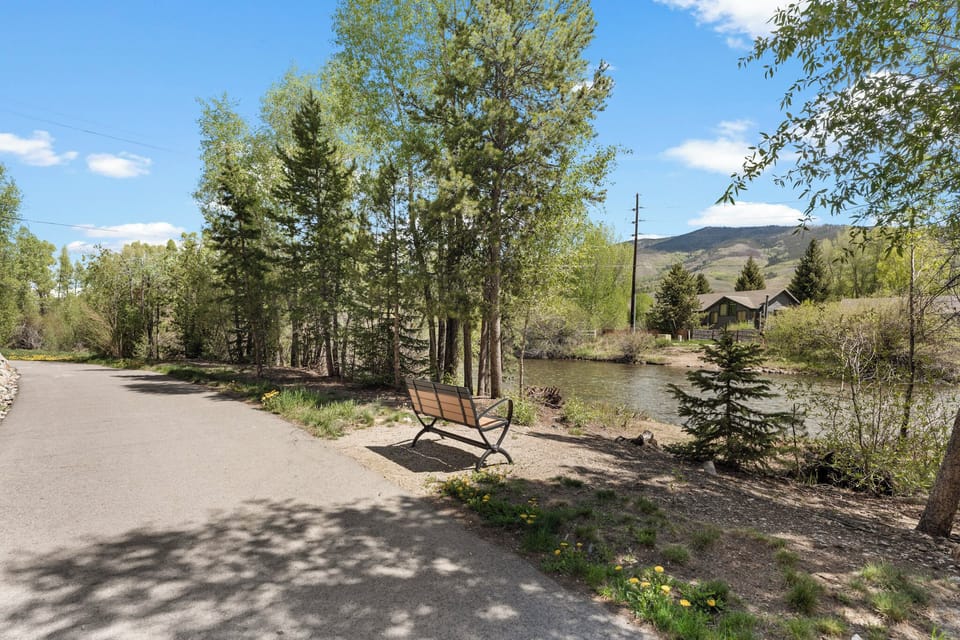 A peaceful riverside path with mountain views and a bench, perfect for strolling through the scenic natural surroundings near the property.