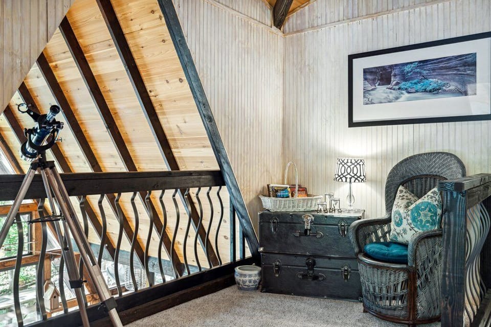 Loft seating nook with a wicker chair, trunk, telescope, and open living-room overlook.