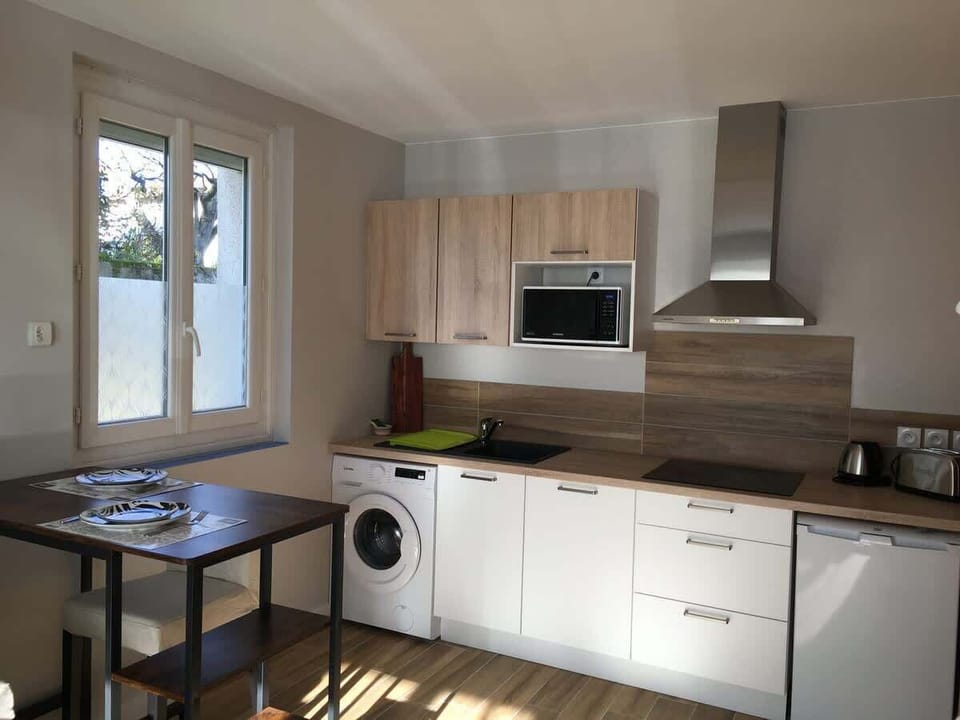 Cuisine ouverte avec plan de travail, lave-linge, hotte et petite table