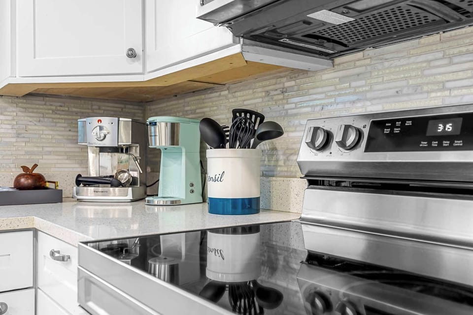 Modern kitchen countertop with coffee makers and cooking utensils next to a stainless steel stove