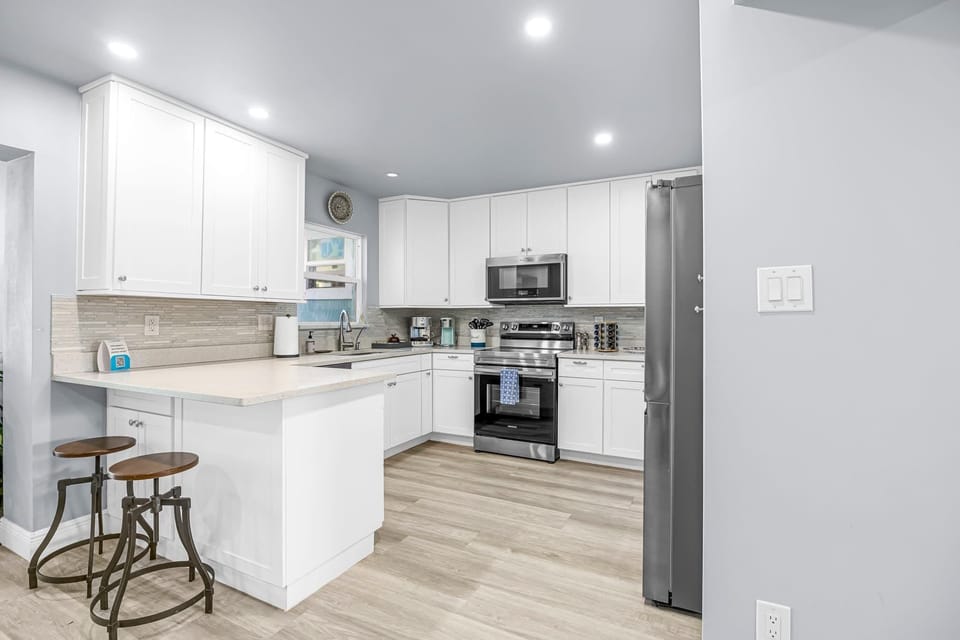 Modern kitchen with white cabinetry, stainless steel appliances, and a breakfast bar with stools.
