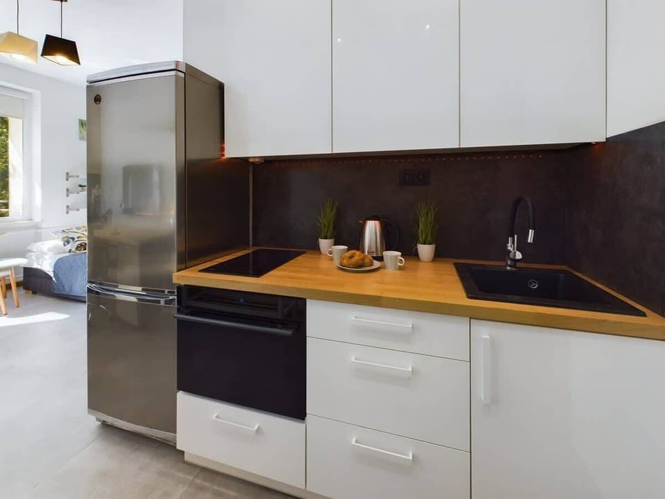A compact kitchenette with white cabinets, black backsplash, and wooden countertops. Everything is neatly arranged for convenient meal prep.
