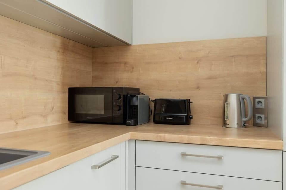 A minimalist kitchen in white and wood tones. Equipped with a coffee maker, toaster, and microwave for everyday convenience.