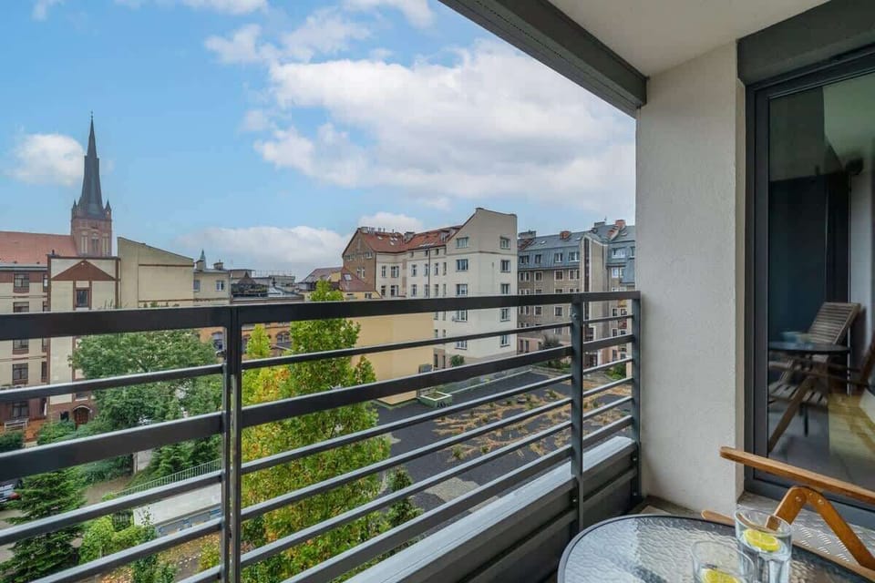 A view from the balcony overlooking charming rooftops and a church tower. Outdoor seating invites you to enjoy fresh air and city views.