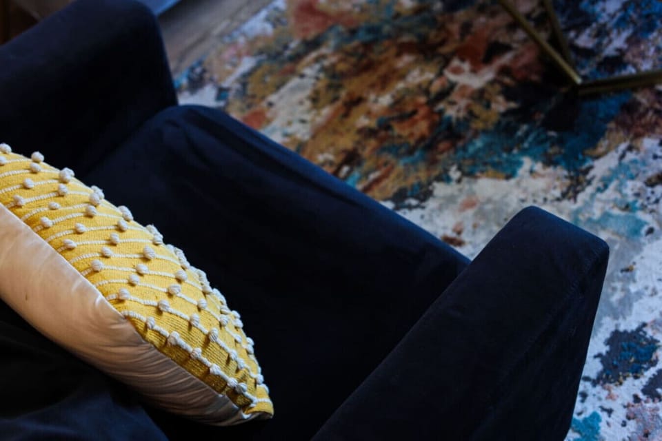 Close-up of blue and yellow decorative pillow on navy velvet sofa with colorful abstract area rug