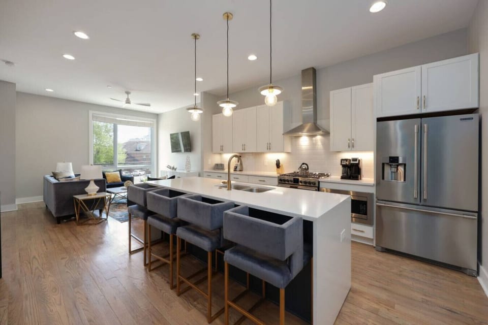 Kitchen with white cabinetry, waterfall island, dark bar stools, stainless steel appliances, and range hood