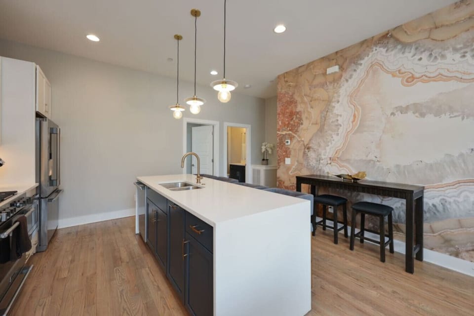 Kitchen with dark island, white quartz countertop, pendant globe lights, and exposed brick accent wall