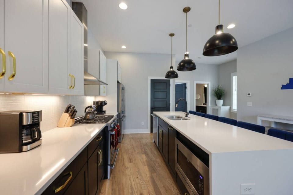 Kitchen from alternate angle with dark lower cabinets, white upper cabinets, black pendants, and island