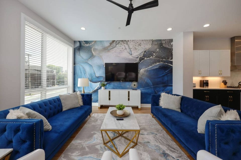 Living room with two royal blue velvet sofas, white armchairs, gold marble coffee table, and stone feature wall