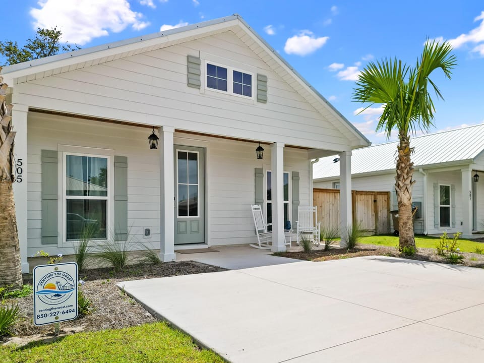 Charming coastal cottage with covered porch welcomes guests to a tranquil vacation retreat surrounded by palm trees and sunshine.