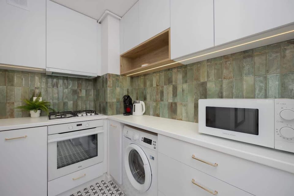 A modern kitchen with white cabinetry, green backsplash, and integrated appliances. The design is compact and well-equipped.