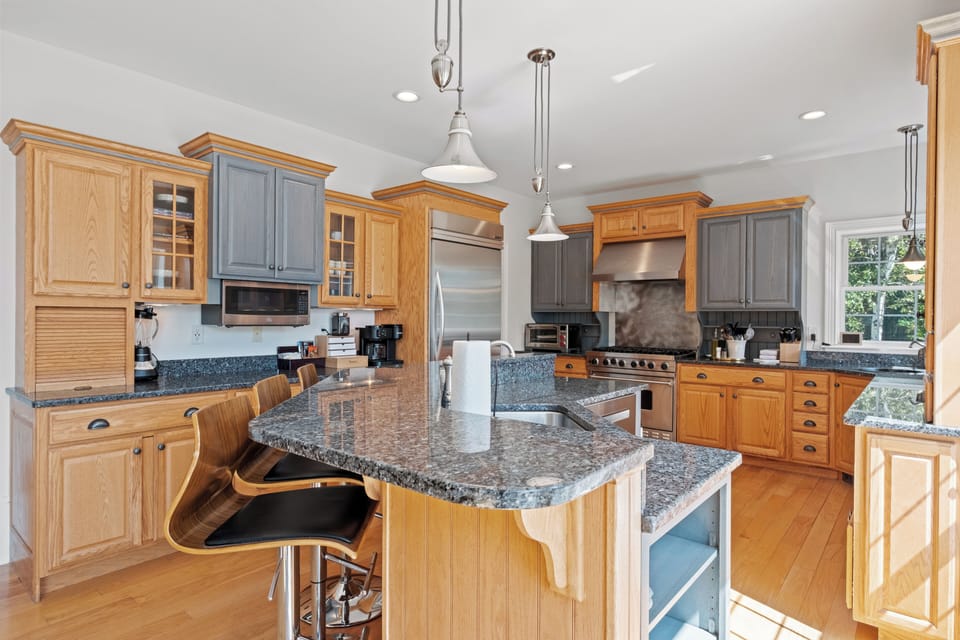 Bright kitchen with granite countertops, stainless steel appliances, and full kitchen equipment. Warm wood tones, cozy breakfast bar, and stylish pendant lighting for a welcoming vibe.