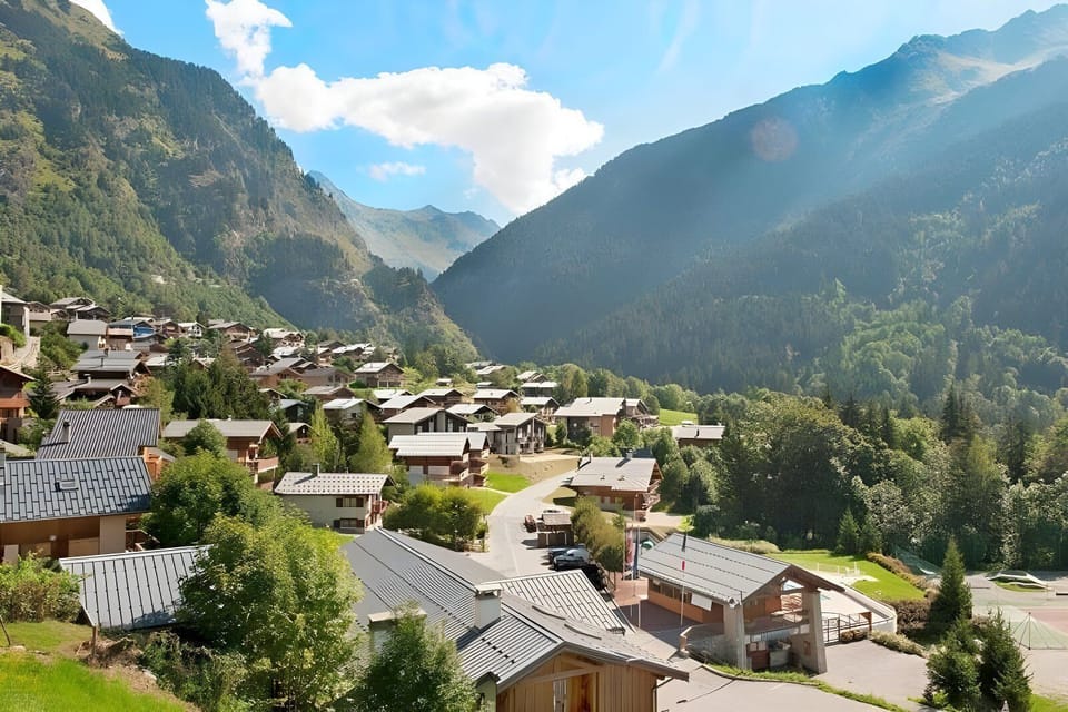 This aerial view showcases the charming village setting of the apartment. The picturesque alpine landscape is dotted with traditional chalet-style homes, surrounded by lush greenery and towering mountains in the background. Enjoy breathtaking views from t