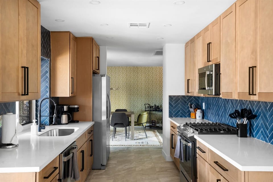 Featuring oak cabinets, a striking blue tile backsplash, and pristine white quartz countertops, all illuminated by bright lighting