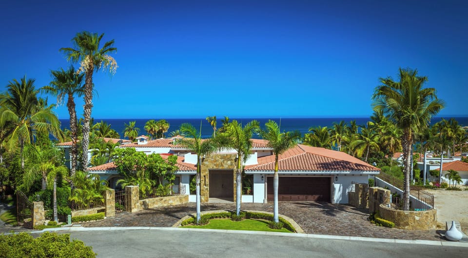 Villa Esperanza front exterior with a palm-lined circular driveway in Palmilla Caleta, Los Cabos.